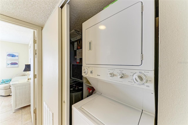 laundry area with stacked washing maching and dryer, light tile patterned floors, and a textured ceiling