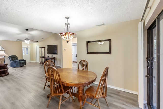 dining space featuring lofted ceiling, hardwood / wood-style flooring, and a textured ceiling