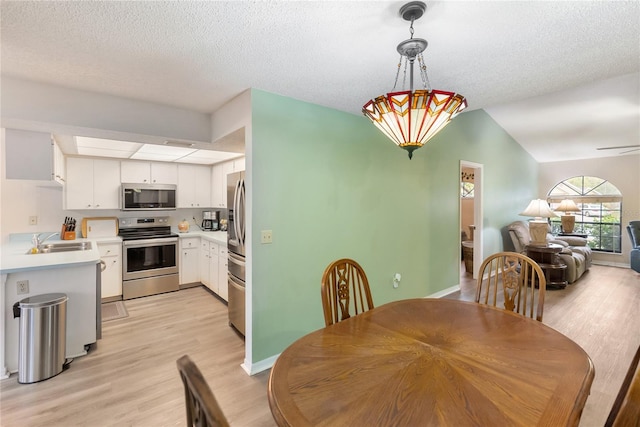 dining space featuring sink, light hardwood / wood-style flooring, a textured ceiling, and vaulted ceiling