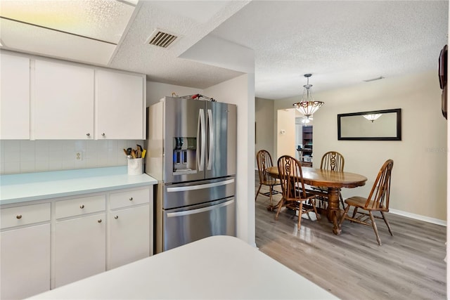 kitchen with pendant lighting, light hardwood / wood-style flooring, a textured ceiling, white cabinets, and stainless steel fridge with ice dispenser