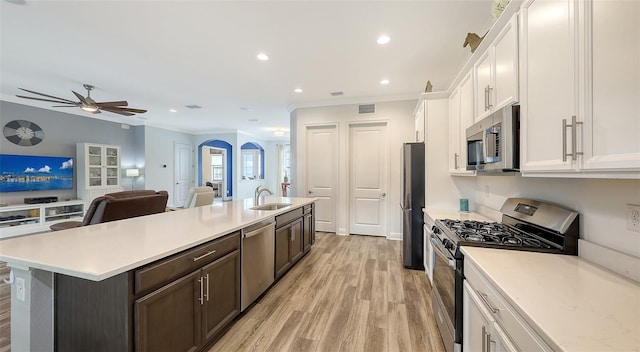 kitchen with white cabinetry, dark brown cabinetry, light hardwood / wood-style floors, stainless steel appliances, and a center island with sink