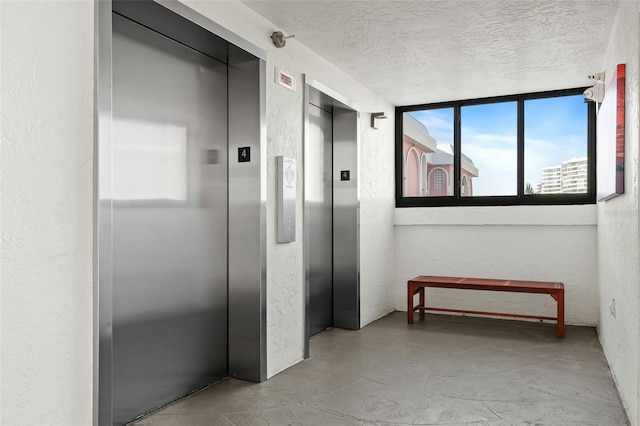 corridor with elevator and a textured ceiling