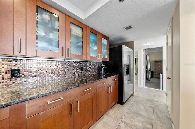 kitchen featuring stainless steel fridge, backsplash, a textured ceiling, and dark stone counters