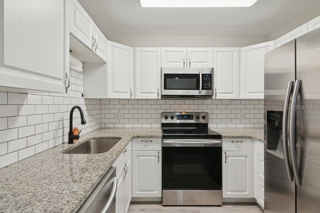 kitchen with stainless steel appliances, sink, white cabinets, and light stone counters