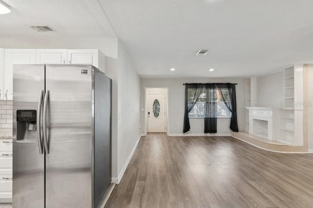 kitchen featuring stainless steel fridge with ice dispenser, a fireplace, hardwood / wood-style floors, and white cabinets