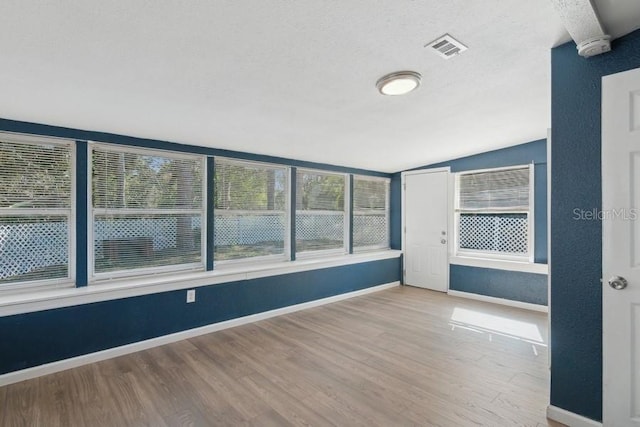 unfurnished room with wood-type flooring, lofted ceiling, and a textured ceiling