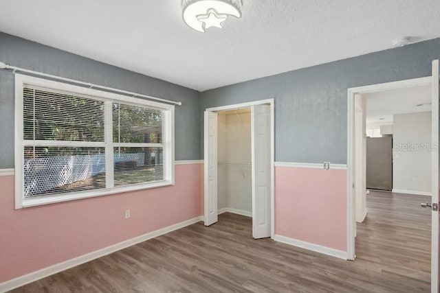 unfurnished bedroom featuring wood-type flooring, stainless steel fridge, a textured ceiling, and a closet