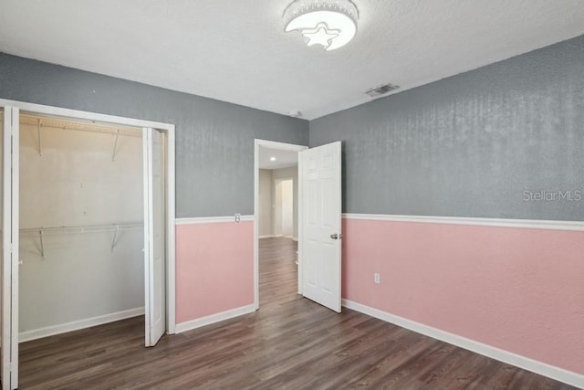 unfurnished bedroom featuring dark wood-type flooring, a closet, and a textured ceiling