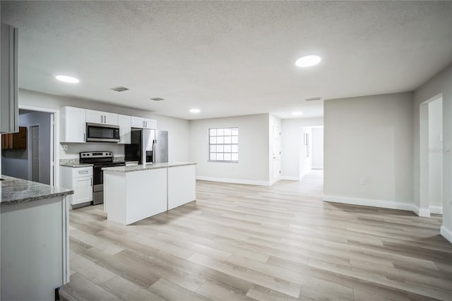 kitchen featuring a kitchen island, white cabinets, stainless steel appliances, light stone countertops, and light wood-type flooring