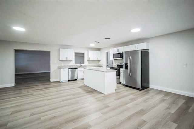 kitchen featuring white cabinetry, stainless steel appliances, light stone counters, light hardwood / wood-style floors, and a kitchen island