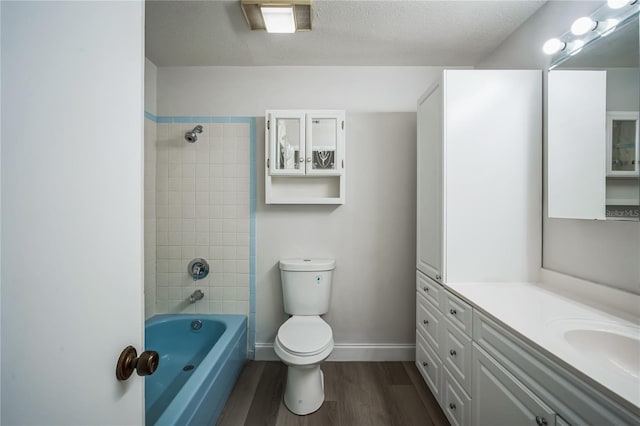 full bathroom featuring tiled shower / bath, hardwood / wood-style floors, vanity, toilet, and a textured ceiling