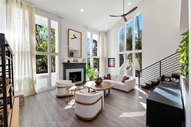 living room featuring high vaulted ceiling, a tile fireplace, light hardwood / wood-style floors, and a healthy amount of sunlight