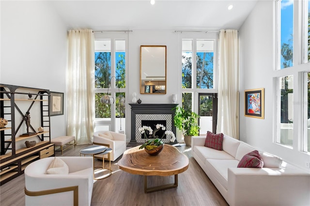 living room featuring a tile fireplace, light hardwood / wood-style flooring, and a high ceiling