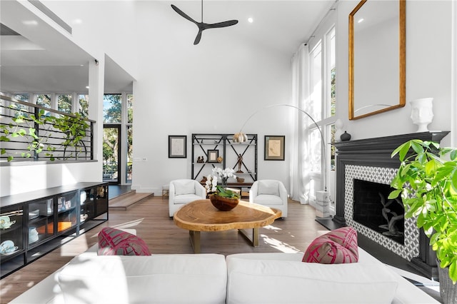 living room with hardwood / wood-style flooring, a tile fireplace, a towering ceiling, and ceiling fan