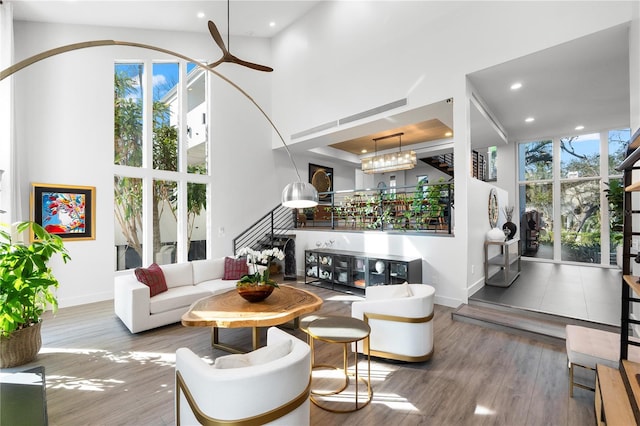 living room with ceiling fan, a towering ceiling, a healthy amount of sunlight, and hardwood / wood-style flooring