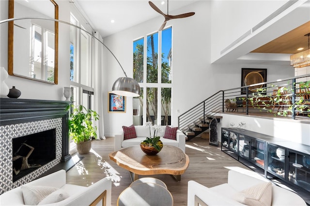 living room with ceiling fan, a fireplace, wood-type flooring, and a high ceiling