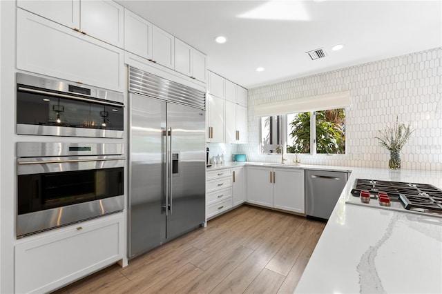 kitchen featuring white cabinets, backsplash, light hardwood / wood-style floors, stainless steel appliances, and light stone countertops