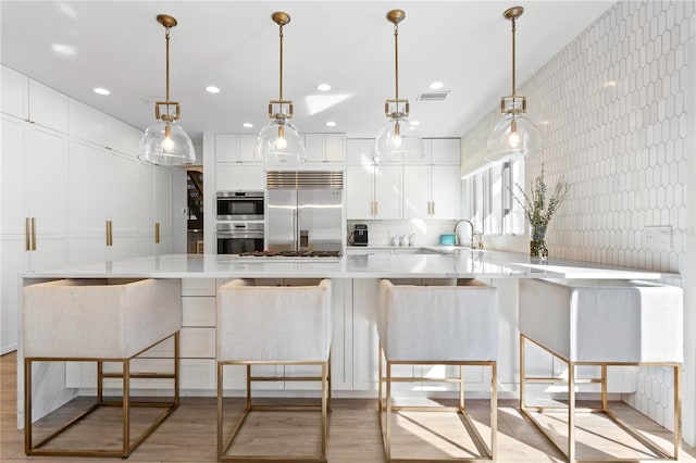 kitchen with stainless steel appliances, kitchen peninsula, white cabinets, and decorative light fixtures