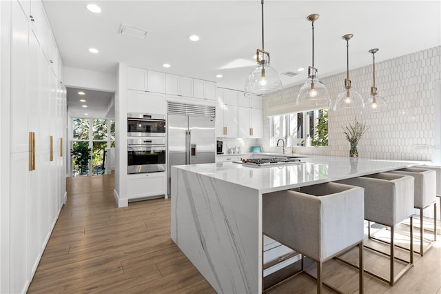 kitchen with white cabinetry, stainless steel appliances, a kitchen breakfast bar, light hardwood / wood-style floors, and decorative light fixtures