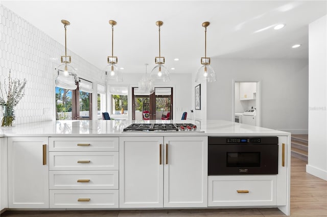 kitchen with black oven, white cabinetry, hanging light fixtures, light stone countertops, and stainless steel gas cooktop