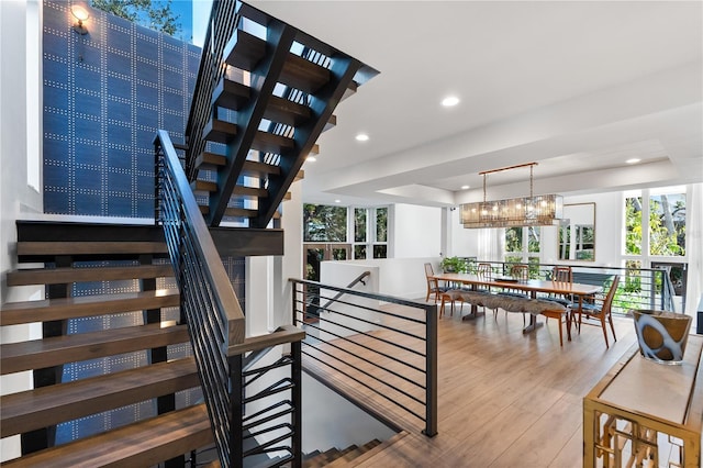 stairway with a raised ceiling, wood-type flooring, and an inviting chandelier