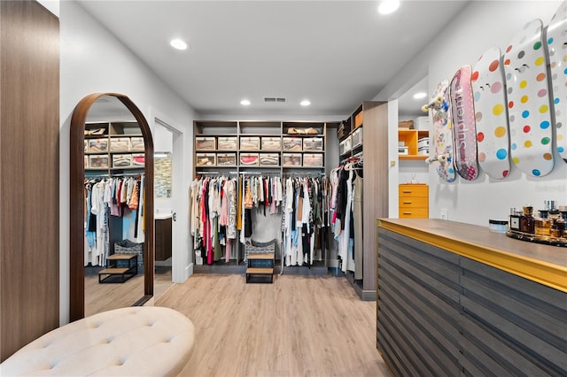 walk in closet with bar area and light wood-type flooring