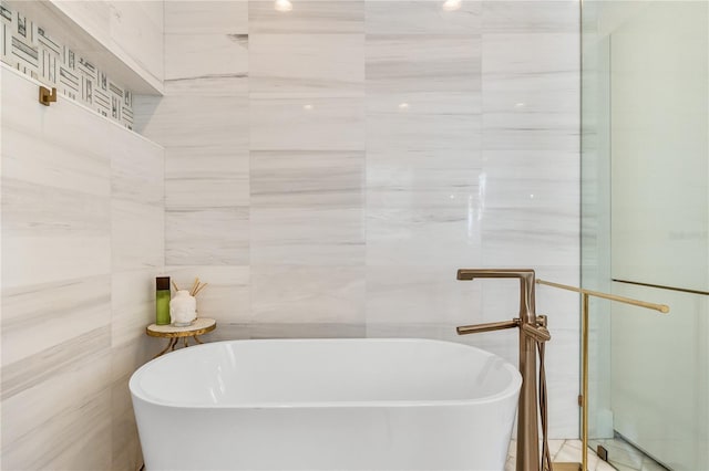 bathroom with a tub to relax in and tile walls