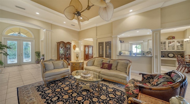 tiled living room with crown molding, a towering ceiling, a raised ceiling, french doors, and ornate columns