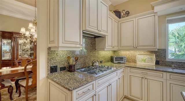 kitchen featuring an inviting chandelier, stainless steel gas stovetop, dark stone counters, cream cabinets, and decorative backsplash