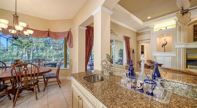 kitchen featuring light tile patterned flooring, sink, crown molding, dark stone countertops, and a notable chandelier