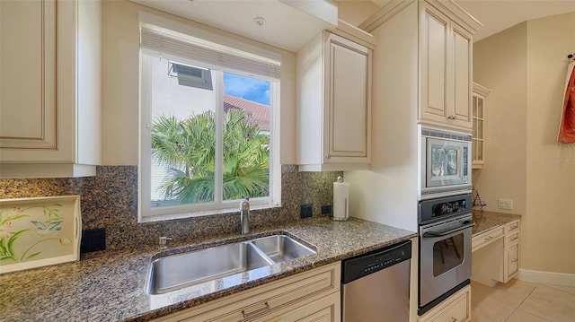 kitchen with sink, stainless steel appliances, cream cabinetry, and dark stone counters