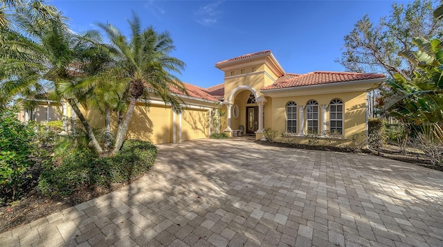 mediterranean / spanish home with a garage, driveway, a tile roof, and stucco siding