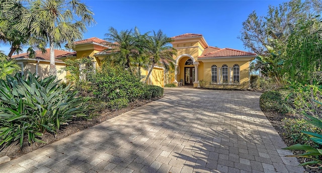 mediterranean / spanish home featuring a garage, decorative driveway, a tiled roof, and stucco siding