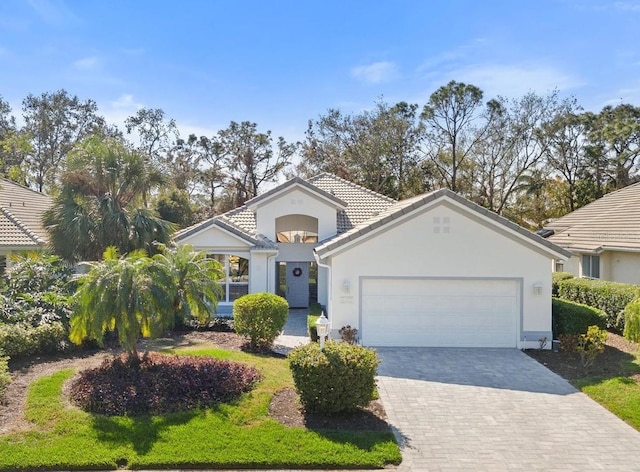 mediterranean / spanish home featuring an attached garage, a tile roof, decorative driveway, and stucco siding