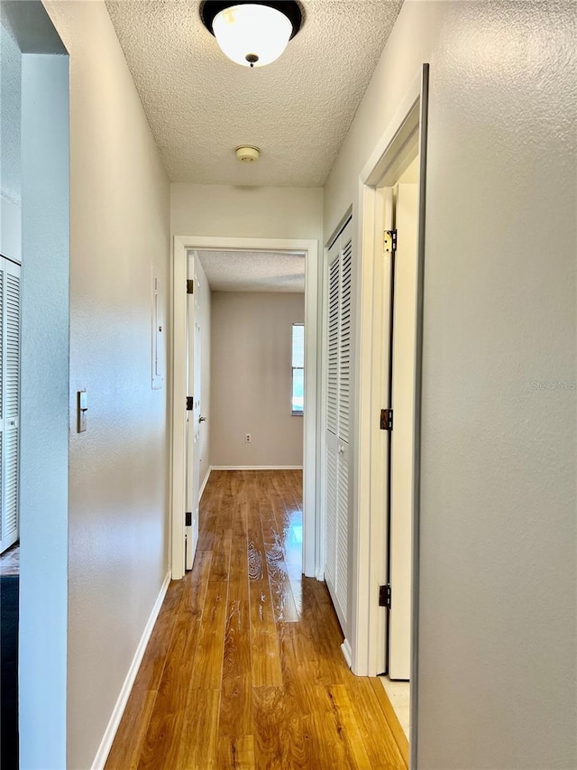 hall with a textured ceiling and light wood-type flooring