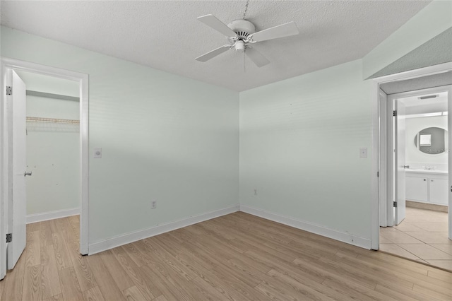 empty room with a textured ceiling, ceiling fan, and light wood-type flooring