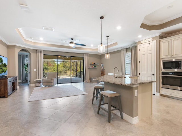 kitchen featuring built in microwave, oven, a kitchen island with sink, a tray ceiling, and light stone countertops