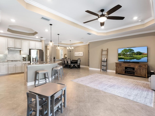 tiled living room with sink, ornamental molding, a tray ceiling, and ceiling fan with notable chandelier