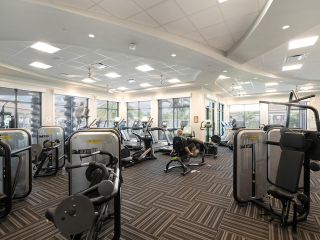 exercise room featuring a paneled ceiling, a healthy amount of sunlight, and dark colored carpet