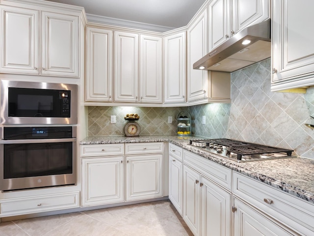 kitchen featuring light tile patterned flooring, light stone counters, backsplash, appliances with stainless steel finishes, and white cabinets