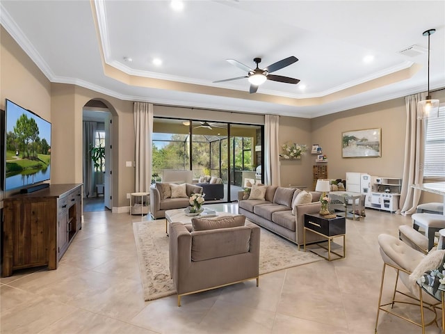 living room featuring light tile patterned floors, a tray ceiling, ornamental molding, and ceiling fan