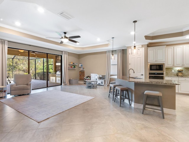 kitchen featuring stone counters, a kitchen island with sink, black microwave, a raised ceiling, and stainless steel oven