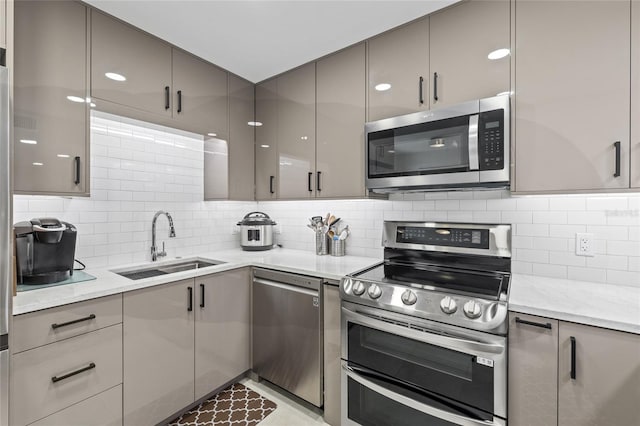 kitchen featuring tasteful backsplash, sink, gray cabinetry, light stone counters, and stainless steel appliances