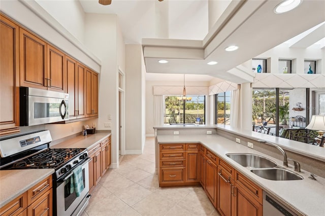 kitchen with sink, appliances with stainless steel finishes, a high ceiling, light tile patterned flooring, and decorative light fixtures