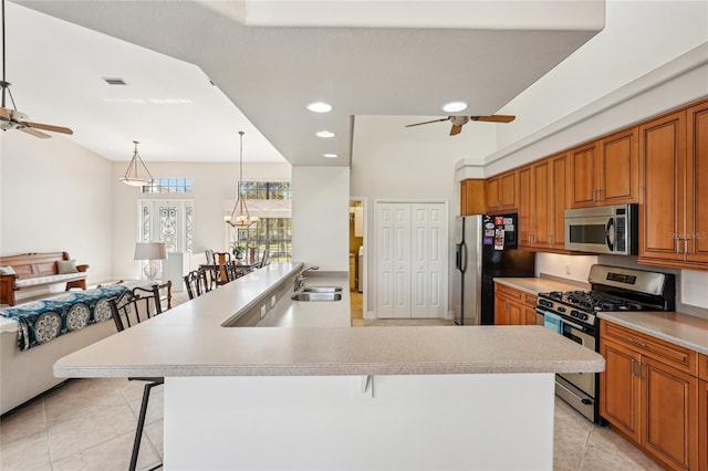 kitchen with decorative light fixtures, light tile patterned floors, appliances with stainless steel finishes, a kitchen breakfast bar, and ceiling fan with notable chandelier