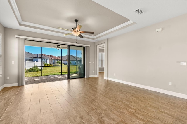 spare room featuring crown molding, ceiling fan, a tray ceiling, and light wood-type flooring