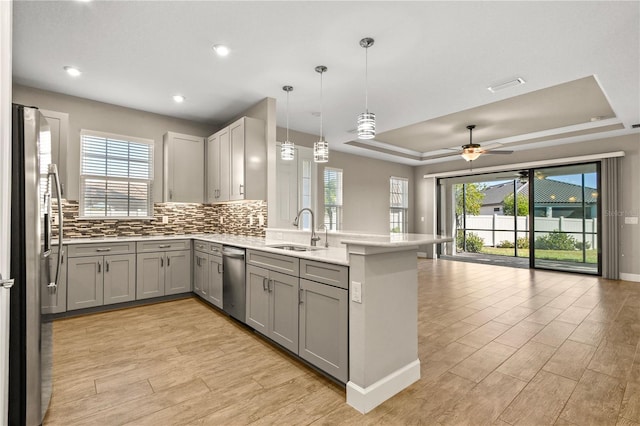 kitchen featuring sink, hanging light fixtures, appliances with stainless steel finishes, a tray ceiling, and gray cabinets