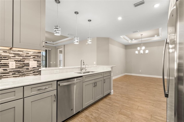 kitchen with sink, gray cabinetry, hanging light fixtures, stainless steel appliances, and a raised ceiling