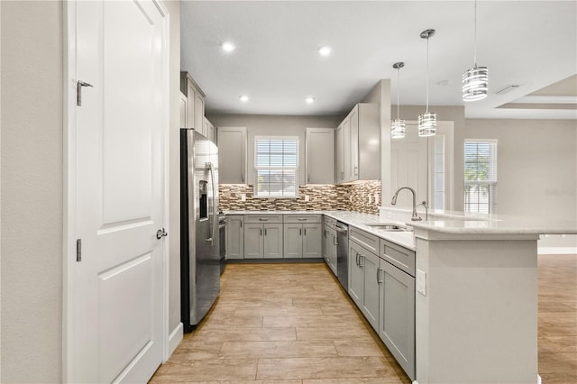 kitchen with appliances with stainless steel finishes, gray cabinetry, hanging light fixtures, backsplash, and kitchen peninsula