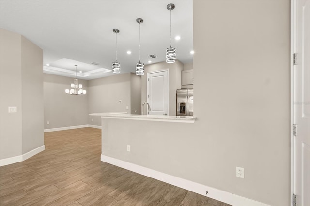 kitchen with stainless steel fridge with ice dispenser, pendant lighting, a chandelier, a tray ceiling, and light hardwood / wood-style flooring